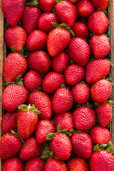 A wooden crate brimming with fresh, ripe strawberries, bursting with vibrant red color and juicy sweetness, ready to eat
