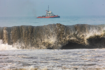 Ocean wave contaminated with oil, with ships in the background attempting to contain the environmental impact