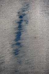 Close-up of beach sand stained with oil residue from an oil spill, showing the environmental impact on the shoreline Oil-stained beach sand with remnants of a petroleum spill