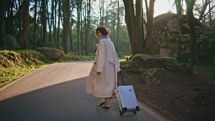 Traveler walking forest road with suitcase illuminated bright autumn sunlight.