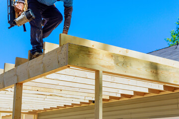 In nailing wooden plank frame together, framer worker uses an air nails hammer to install beams