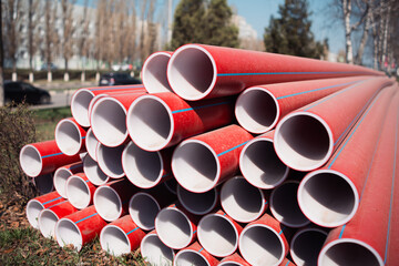 Stacked Red Plastic Pipes Beside Roadway On Sunny Day
