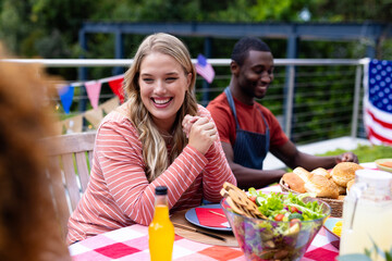 Happy diverse group of friends talking and having dinner at balcony with flags of usa