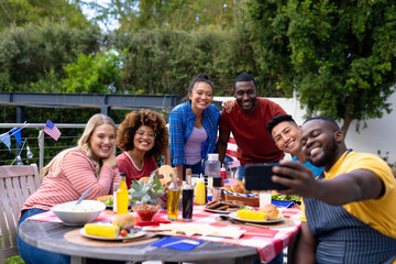 Happy diverse group of friends taking selfie and having dinner at balcony with flags of usa