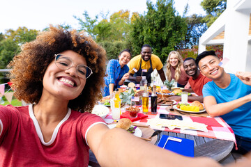 Portrait of happy diverse group of friends taking selfie and having dinner with flags of usa