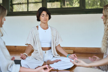 Three diverse women meditating sitting together with eyes closed in circle in yoga poses at body...