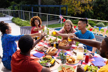 Happy diverse group of friends cheering with drinks and having dinner with flags of usa