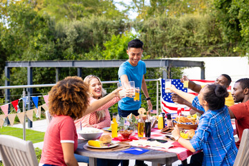 Happy diverse group of friends cheering with drinks and having dinner with flags of usa