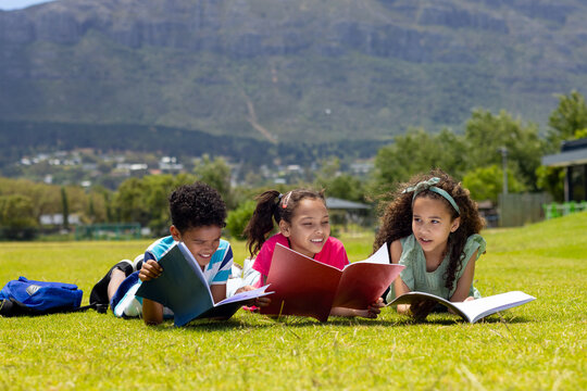 Biracial boy and girls are reading books on a sunny grass field