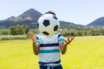 Biracial boy plays with a soccer ball outdoors, surrounded by greenery and mountains