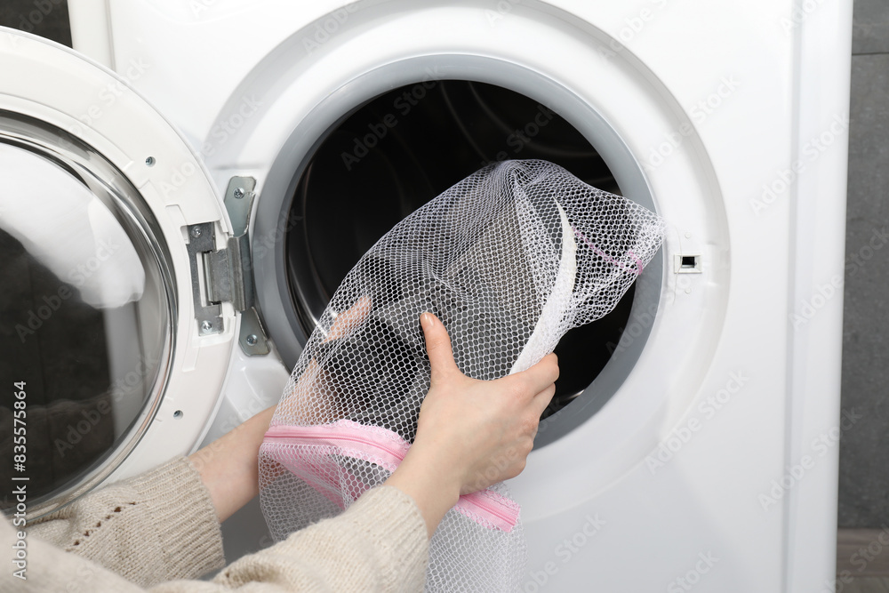 Wall mural Woman putting stylish sneakers into washing machine, closeup