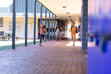 Three biracial girls are running joyfully down a school corridor with copy space