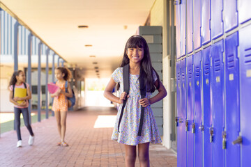 Biracial girl with long dark hair smiles in a school hallway with copy space
