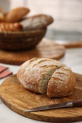 Wicker bread basket with freshly baked loaves and knife on white marble table in kitchen