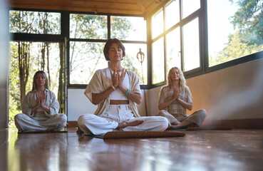 Young women doing breathing exercises at group class yoga meditation session sitting in yoga pose on wooden floor in studio with eyes closed practicing pranayama during retreat therapy.