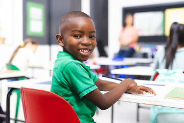 Young African American boy sits at classroom desk in school, smiling at camera