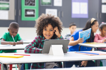 Young biracial girl with curly hair using tablet in classroom