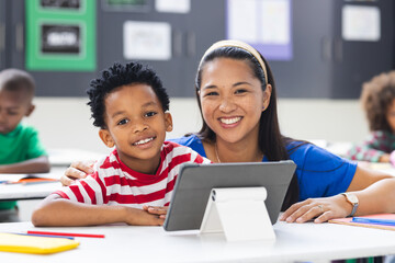 In a classroom, a biracial teacher and her African American child watch a tablet together