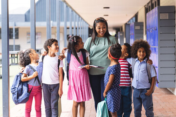 A middle-aged African American teacher with six diverse children outdoors at school