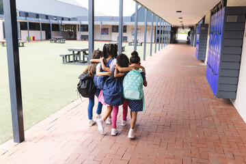 In school, four young biracial girls are walking closely together outdoors