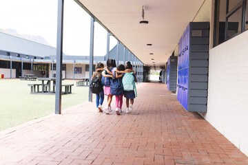 In school, four young biracial girls are walking together outdoors, copy space