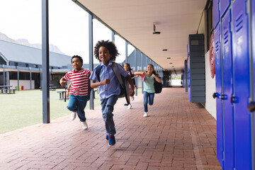 In school, diverse group of young students running in hallway outdoors, copy space