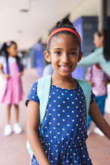 Young biracial girl wearing polka-dot dress and backpack is smiling outdoors