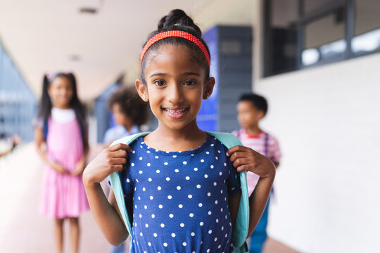 In school, young biracial girl with blue polka dot dress is smiling outdoors