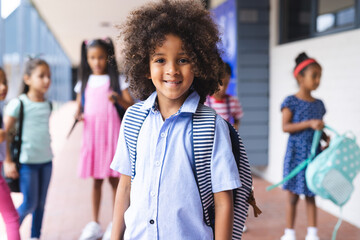 In school, outdoors, young biracial girl with curly hair is standing, smiling