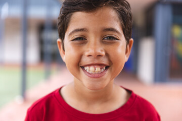 In school, young biracial male student wearing a red shirt is smiling outdoors