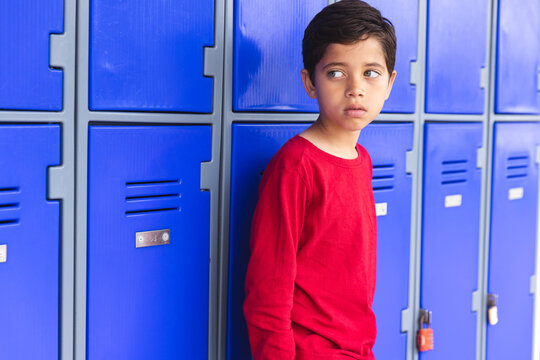 In school, young biracial male student leaning against blue lockers outdoors - Powered by Adobe