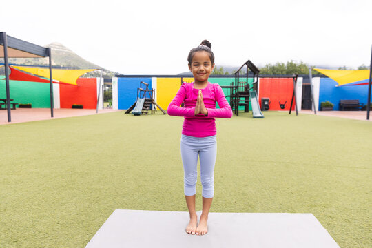 In school playground outdoors, a biracial young girl is practicing yoga - Powered by Adobe