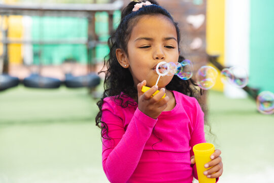 In school outdoors, young biracial girl is blowing bubbles