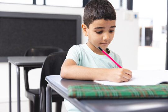 In school, young biracial boy focusing on writing in a notebook in the classroom