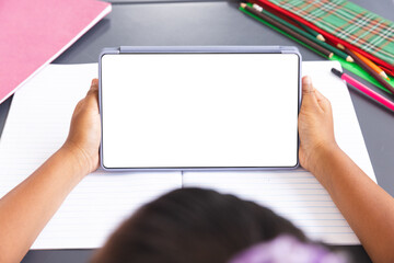 Biracial girl in classroom holds tablet with blank screen for copy space