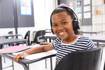 In school, young biracial girl wearing headphones is smiling at camera in the classroom - Powered by Adobe