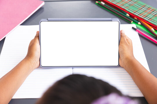 Biracial girl in classroom holds tablet with blank screen for copy space - Powered by Adobe