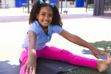 Biracial girl stretches on a mat at school
