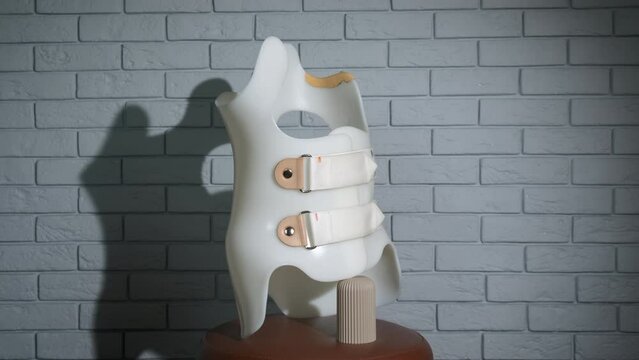 Plastic corrective corset. A plastic white scoliosis corrector stand on the chair against wall.
