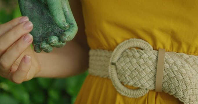 Close-up of a woman hand gently holding arm of sculpture in a garden.