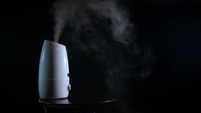 Dark room with working air diffuser. A view of dark room with aroma diffuser working with white steam indoor.