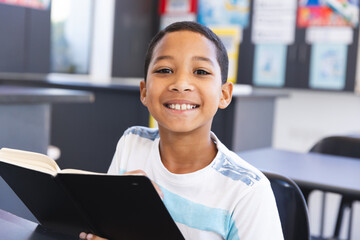 Biracial boy reading a book in the classroom at school