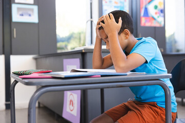 Biracial boy studying in a classroom at school, with copy space