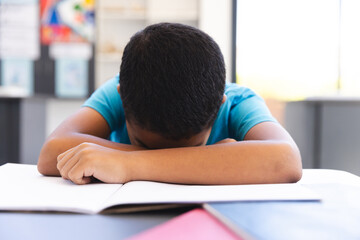 Biracial boy studying in a classroom, head resting on arms at school