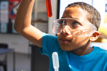 Biracial boy examines a test tube in a school science lab