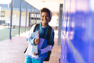 Smiling biracial boy stands by school lockers, with copy space