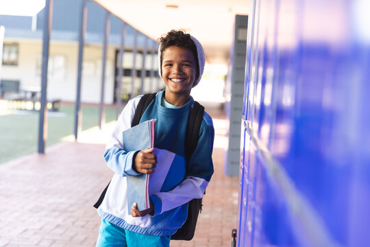 Smiling biracial boy stands by school lockers, with copy space - Powered by Adobe