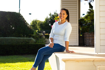 Outdoors, biracial woman in her late thirties sitting on porch steps, smiling warmly