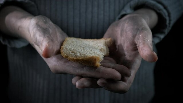 Tired poor hands with bread. A view of tied female hands with a piece of bread against black background.