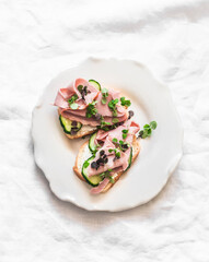 Delicious breakfast, snack, tapas - sandwiches with ham, cucumber and microgreens on a light background, top view